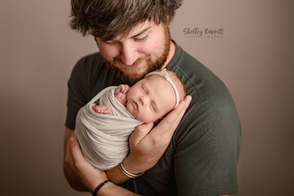Dad holding his sleeping newborn daughter in a timeless studio portrait