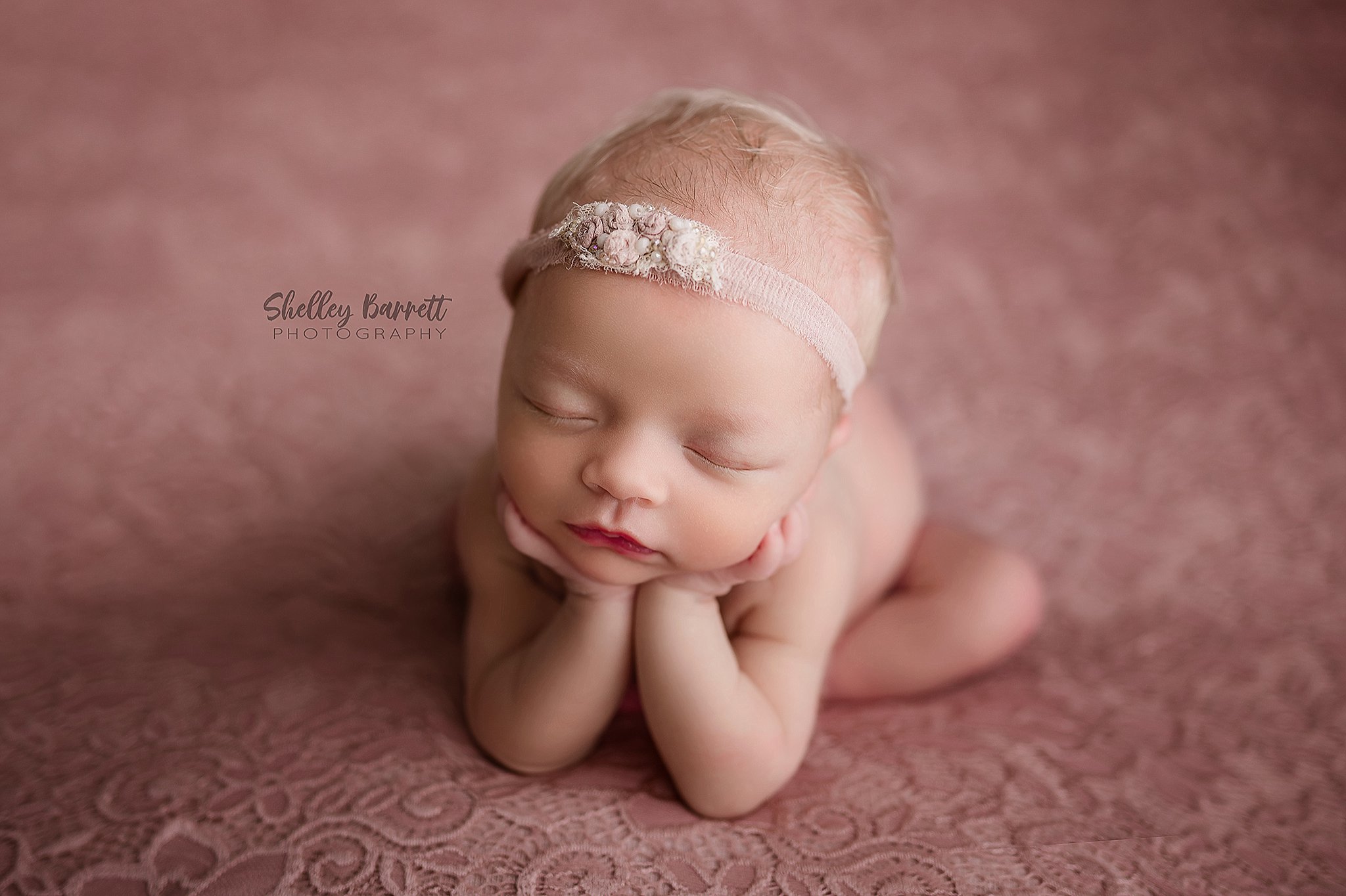 Newborn baby sleeping peacefully in a Trussville newborn photography studio in froggy pose on pink lace
