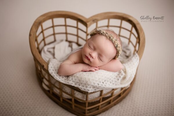 Sleeping summer newborn photographed by a Birmingham newborn photographer in heart basket with flowery headband