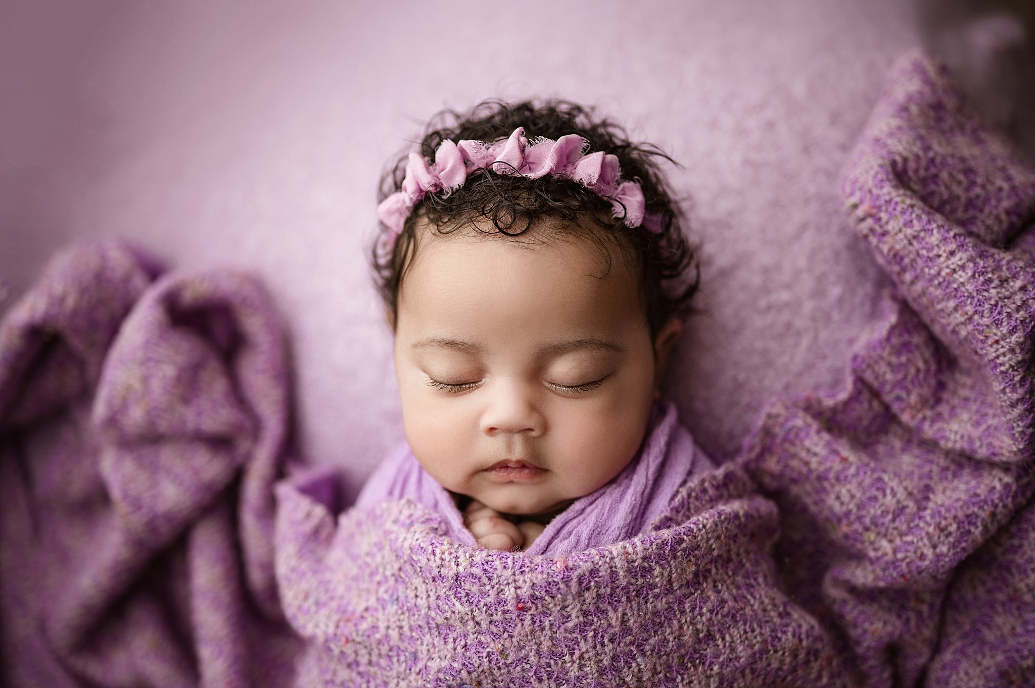Newborn baby girl making a sweet sleeping facial expression while looking toward the camera during a Birmingham newborn photography session.